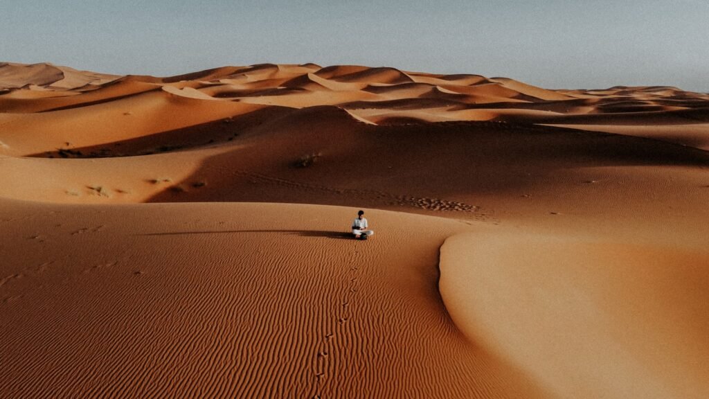 A lone figure walks across vast desert sand dunes. morocco tours for seniors